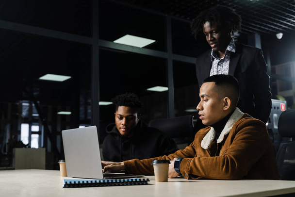 Tiimityötä verkossa kannettavalla tietokoneella. Musta afrikkalainen ja aasialainen kollega. 3 monikansallista liikemiestä katselee videoneuvottelua kollegoiden ja työnantajan kanssa - Valokuva, kuva
