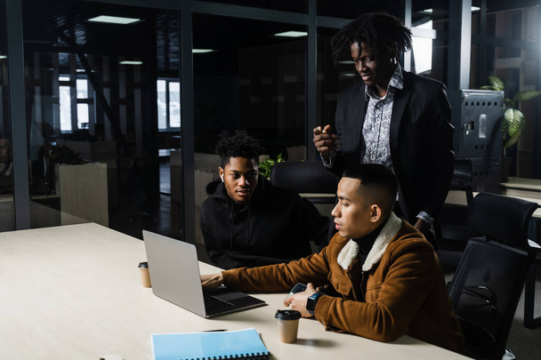 Командная работа онлайн с ноутбуком. Чёрные африканские и азиатские коллеги. 3 мультиэтнических бизнесмена смотрят видеоконференцию с коллегами и работодателем - Фото, изображение