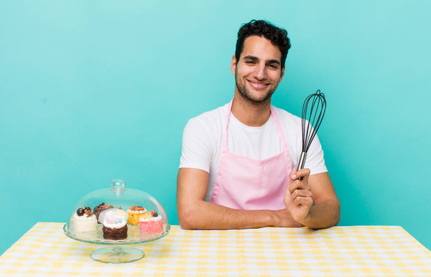 hispanic handsome man smiling happily with a hand on hip and confident. home made cakes cocnept - Fotoğraf, Görsel