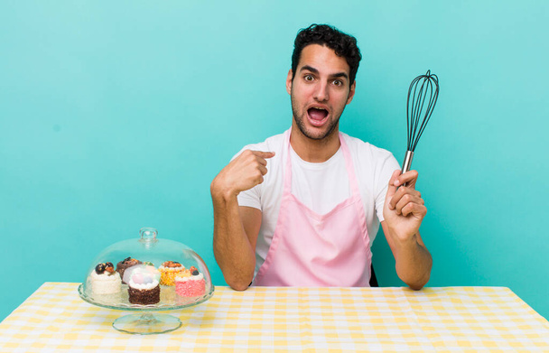 hispanic handsome man looking shocked and surprised with mouth wide open, pointing to self. home made cakes cocnept - Fotoğraf, Görsel