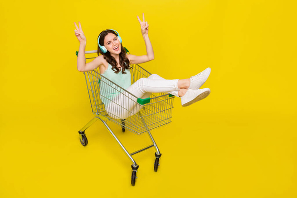 Full body portrait of crazy lady sit trolley show v-sign enjoy wireless stereo song isolated on yellow color background - Zdjęcie, obraz