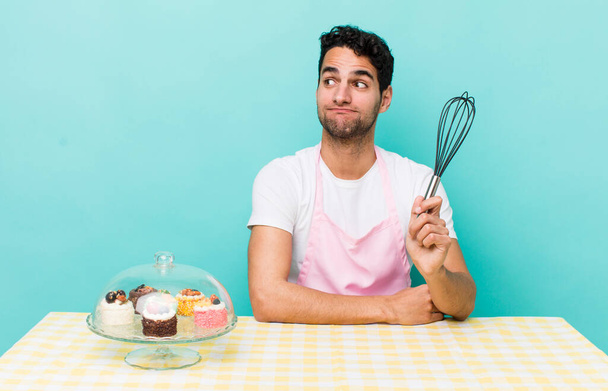 hispanic handsome man shrugging, feeling confused and uncertain. home made cakes cocnept - Fotoğraf, Görsel