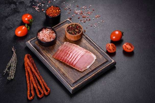 Smoked ham on a dark concrete table with addition of fresh aromatic herbs and spices, natural product from organic farm - Фото, зображення