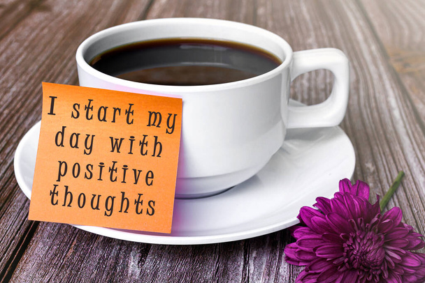 Motivational quote written on stick note with white coffee cup and purple flower - I start my day with positive thoughts. - Photo, Image