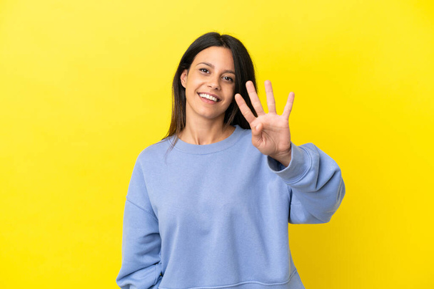 Νεαρή καυκάσια γυναίκα απομονωμένη σε κίτρινο φόντο ευτυχισμένη και μετρώντας τέσσερα με δάχτυλα. - Φωτογραφία, εικόνα