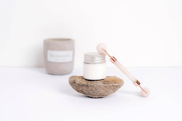 Cream in glass jar with face roller massager on natural stone. Aroma candle on the background. Natural skincare concept. Selective focus. - Photo, Image