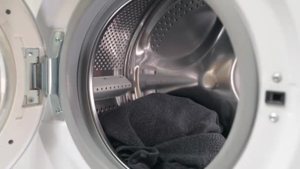 Hands putting black clothes into the washing machine and closing the door - Footage, Video