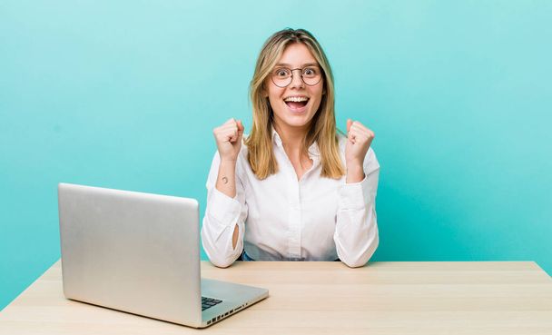 pretty blonde woman feeling shocked,laughing and celebrating success. business and desk concept - Фото, изображение