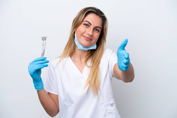 Dentista mulher segurando ferramentas isoladas no fundo branco apertando as mãos para fechar um bom negócio - Foto, Imagem