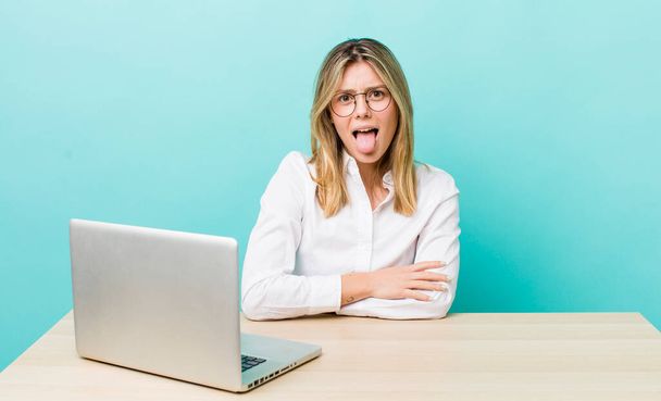 pretty blonde woman with cheerful and rebellious attitude, joking and sticking tongue out. business and desk concept - Photo, Image