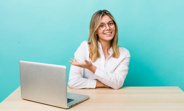 pretty blonde woman smiling cheerfully, feeling happy and showing a concept. business and desk concept - Фото, изображение