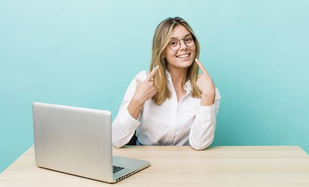 pretty blonde woman smiling confidently pointing to own broad smile. business and desk concept - Φωτογραφία, εικόνα