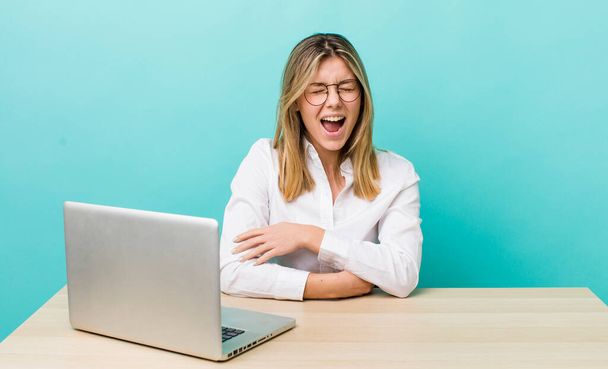 pretty blonde woman shouting aggressively, looking very angry. business and desk concept - Foto, Imagen