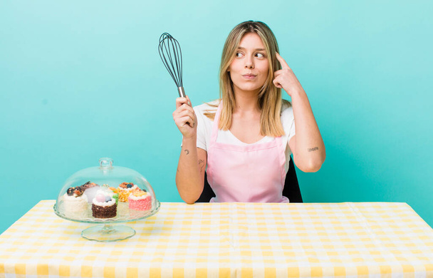 pretty blonde woman feeling puzzled and confused, scratching head. homemade cake concept - Photo, Image