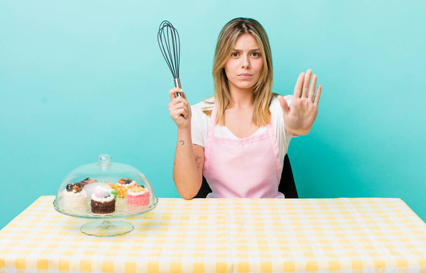 pretty blonde woman looking serious showing open palm making stop gesture. homemade cake concept - Фото, зображення
