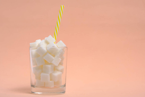 Glass with refined sugar cubes and a drinking tube on a beige background - Photo, image