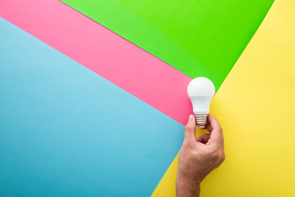 Hand mit weißer Glühbirne auf farbigem Hintergrund in Pastellfarben. Minimalistisches Konzept, kluges Ideenkonzept, - Foto, Bild
