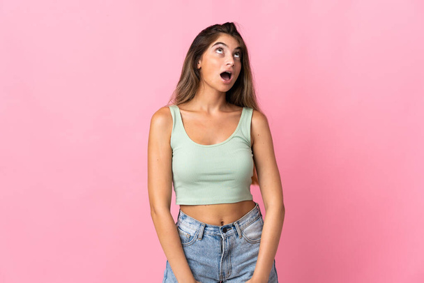 Young caucasian woman isolated on pink background looking up and with surprised expression - Фото, зображення