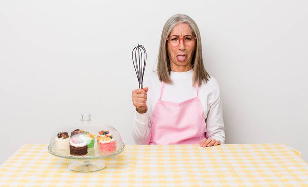 senior  gray hair woman feeling disgusted and irritated and tongue out. homemade cakes concept - Foto, Imagen