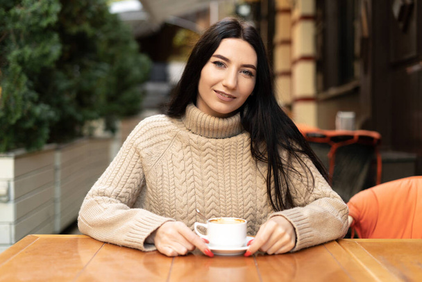 Πορτρέτο μιας χαμογελαστής γυναίκας σε ένα καφέ δρόμο με ένα φλιτζάνι καφέ, επιχειρηματικό τρόπο ζωής, πρωινό σε εξωτερικούς χώρους, αστική έννοια του τρόπου ζωής - Φωτογραφία, εικόνα