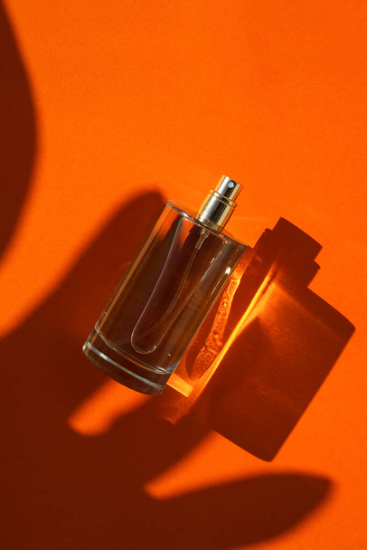 Διαφανές μπουκάλι άρωμα σε πορτοκαλί φόντο. Παρουσίαση αρώματος με το φως της ημέρας. Trending έννοια σε φυσικά υλικά παλάμη φύλλα σκιά. Η ουσία των γυναικών και των ανδρών. - Φωτογραφία, εικόνα