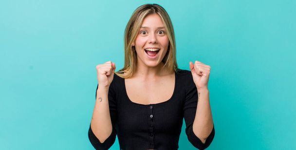young pretty blonde woman feeling shocked, excited and happy, laughing and celebrating success, saying wow! - Foto, Imagen