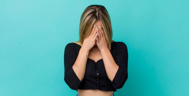 young pretty blonde woman feeling sad, frustrated, nervous and depressed, covering face with both hands, crying - Foto, afbeelding