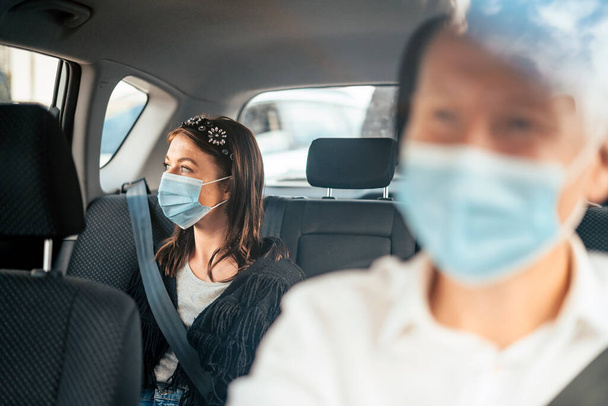 Bir taksinin arka koltuğunda oturan koruyucu maskeli bir kadın. - Fotoğraf, Görsel