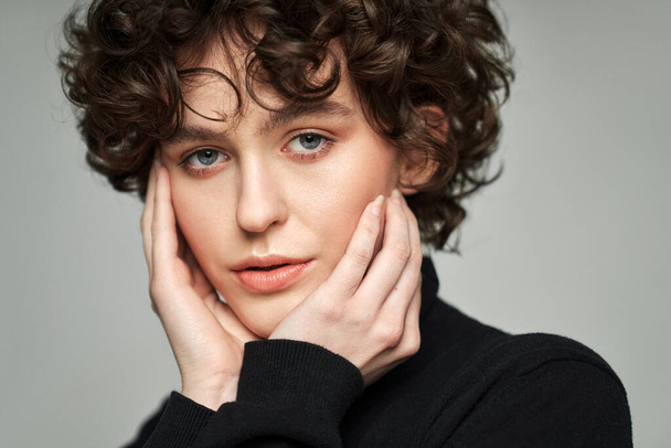 Portrait of brunette with curls wear high neck jumper touching cheeks - Photo, image
