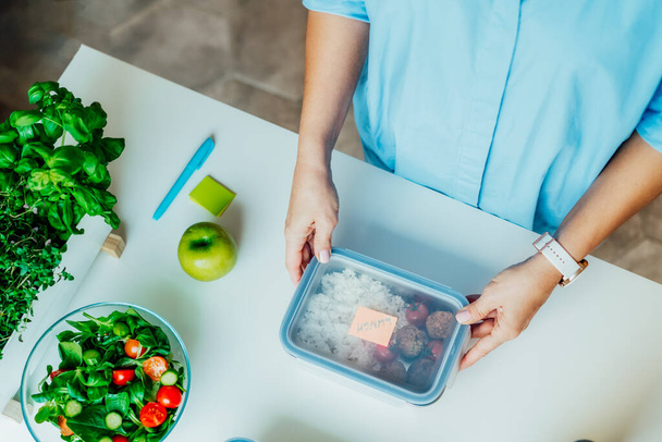 Healthy diet plan for weight loss, daily ready meal menu. Close up woman putting note on lunch box cooked in advance, ready to eat for lunch. Balanced portion with healthy dish. Pre-cooking concept - Foto, imagen