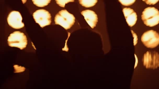 Feiernde Menge tanzt Rockkonzert im Scheinwerferlicht. Aufgeregte Menschen springen auf. - Filmmaterial, Video