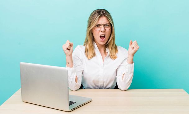 pretty blonde woman shouting aggressively with an angry expression. business and desk concept - Foto, immagini