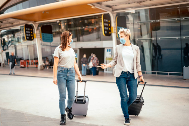 Utazó nők védőmaszkban beszélgetnek, amikor elhagyják a repülőteret a célállomáson - Fotó, kép