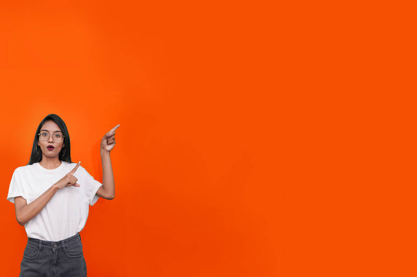 young asian indian woman wearing white t-shirt against orange background pointing finger right side of herself. - Fotoğraf, Görsel
