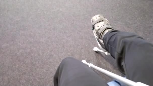 Hombre europeo bruja Aquiles ruptura tendón sentado en la sala de espera del hospital después de la operación con zapato especial y muletas en la sala de espera vacía para la rehabilitación médica después de la emergencia - Imágenes, Vídeo