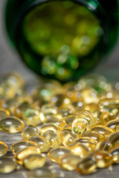 Close up of a green bottle of vitamin gel capsules spilt on a grey wood board with shallow depth of field - Foto, afbeelding