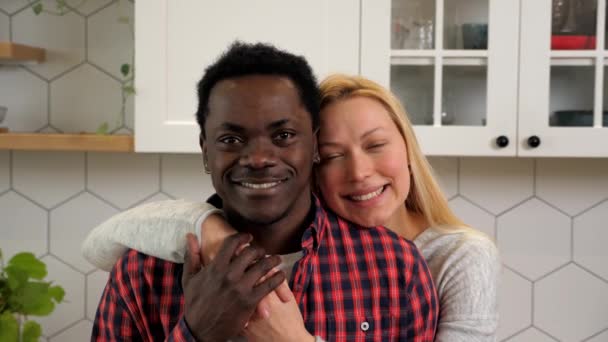 Portrait smiling multiethnic couple hugging looking camera at home kitchen - Filmati, video
