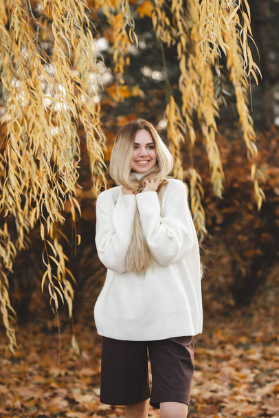 Long-haired blonde on the river bank. Happy young girl relaxes on an autumn day - Фото, зображення