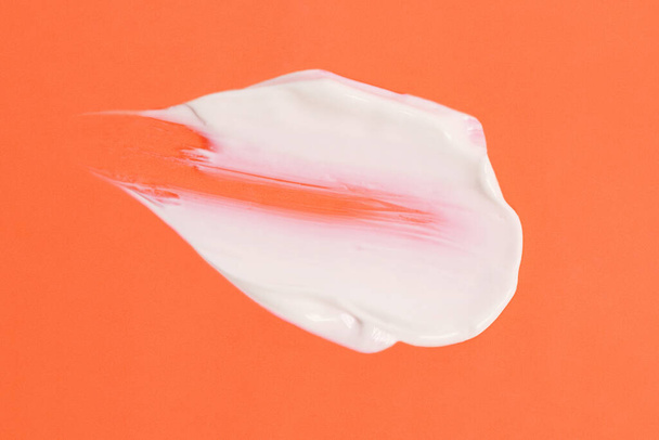 Αφηρημένη επίχρισμα της λευκής καλλυντικής κρέμας στο πορτοκαλί φόντο, αφηρημένη μορφή. - Φωτογραφία, εικόνα