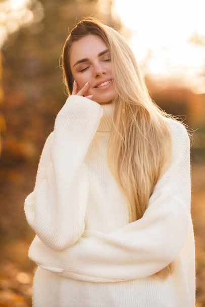 Portret van een charmante blonde met een prachtige glimlach. Meisje in een witte trui - Foto, afbeelding