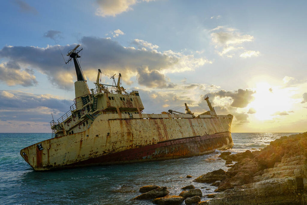 egy nagy, rozsdás hajóroncs egy sziklás parton, gyönyörű naplemente háttér mellett. - Fotó, kép
