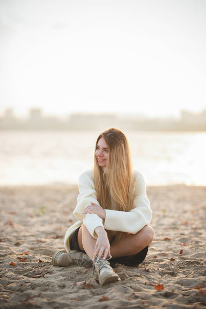 Aantrekkelijk blond in een witte trui op een achtergrond van herfstkleuren - Foto, afbeelding