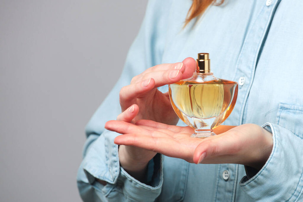 Perfume bottle in hands of woman wearing blue jeans wear - Foto, Bild