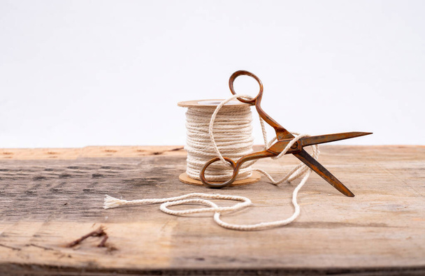 vieux ciseaux ouverts et rouillés, reposant sur une bobine de fil sur une table en bois avec un fond blanc  - Photo, image