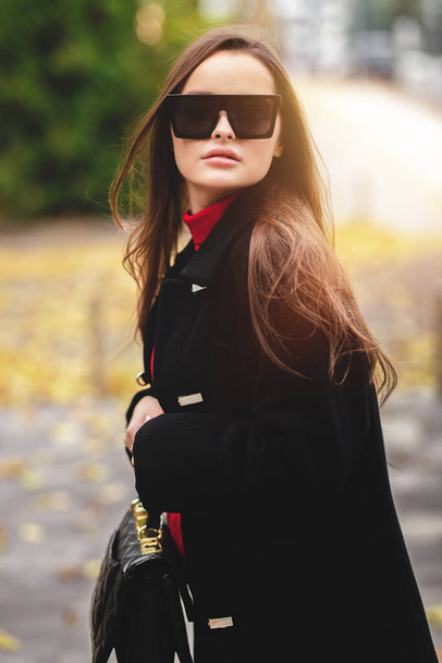 Ceketli ve şık gözlüklü çekici bir genç kızın moda portresi. Ilık sonbahar gölgeleri. - Fotoğraf, Görsel