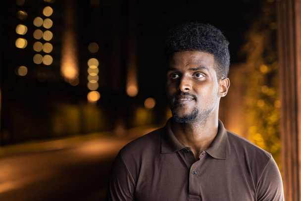 Egy fiatal, jóképű fekete férfi portréja a városban éjszaka. - Fotó, kép