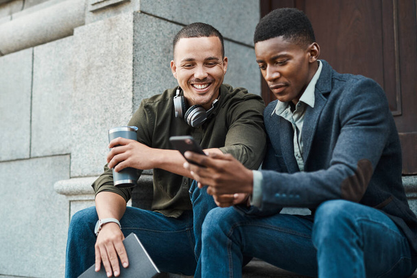 Pracuj tam, gdzie motywuje cię do tego. Zdjęcie dwóch młodych biznesmenów korzystających ze smartfona na tle miejskim. - Zdjęcie, obraz