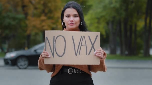 Joven activista hispana seria de pie al aire libre protestando manifestando pancarta con inscripción no vax muestra pancarta de cartón de manifestante contra prohibición de vacunación negándose a inmunizar - Metraje, vídeo