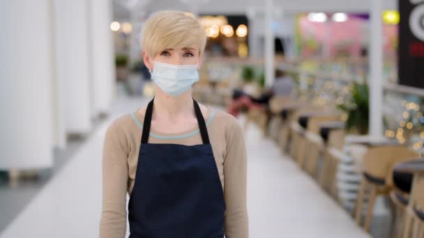 Friendly caucasian masked woman female waitress in medical face protective mask restaurant cafe kitchen bar worker looking at camera welcoming gesture come here approach welcome inviting invite client - Footage, Video