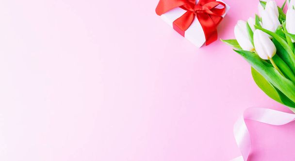 Moederdag cadeau. Voorjaar witte tulp bloem, cadeau met rood lint op platte lay roze achtergrond. Valentijnsdag, verjaardag, vrouwen of trouwdag concept - Foto, afbeelding